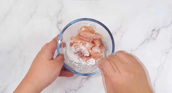 Chicken and cornstarch in a bowl being mixed with a spoon. 