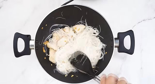 Rice vermicelli noodles added to the wok with chicken and garlic. 