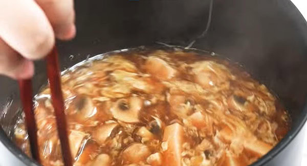 Beaten eggs being added into the pot and stirred with a pair of chopsticks. 