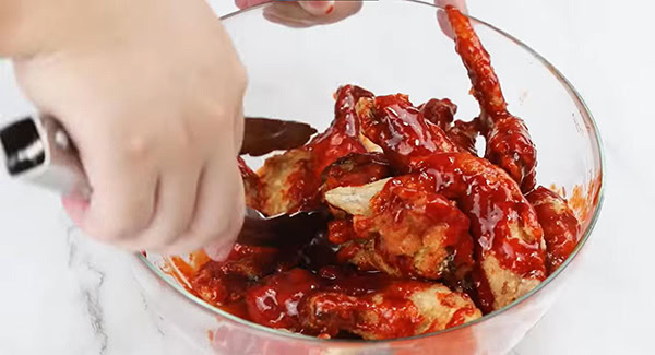 Deep fried chicken wings being tossed in the Korean fried chicken sauce in bowl. 