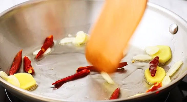 Dried red chilies and sliced ginger sauteed in  a pan.