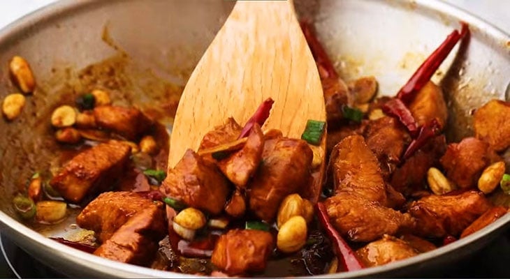 Adding scallions and Kung Pao sauce to a pan. 