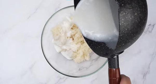 Coconut milk being poured into a bowl of glutinous rice. 