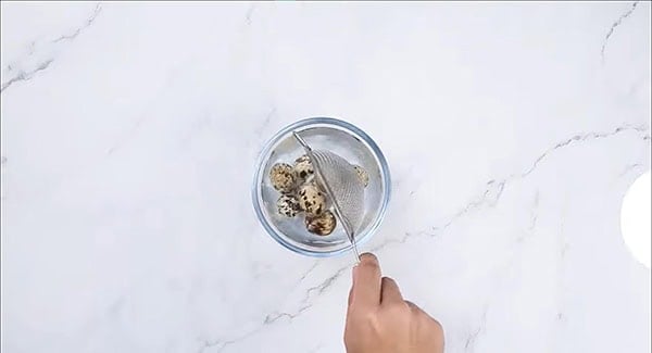 Quail eggs being transferred into a bowl of cold water. 