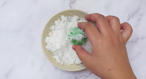 Onde-onde balls being rolled around in grated coconut in a bowl. 