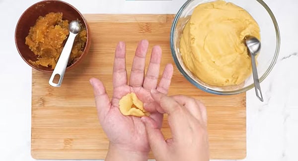 Edges of the flattened dough being pinched together with pineapple filling in middle. 