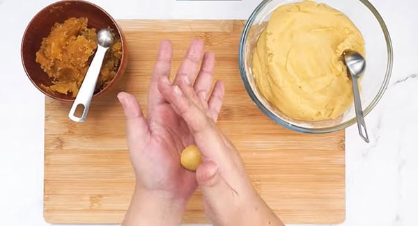 Pineapple cookie dough with filling being rolled into a ball. 