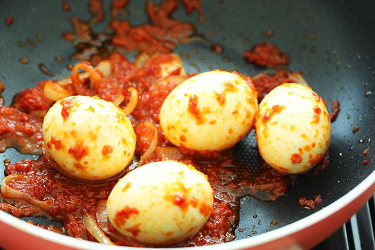 Hard boiled eggs being mixed and coated with the sambal paste.