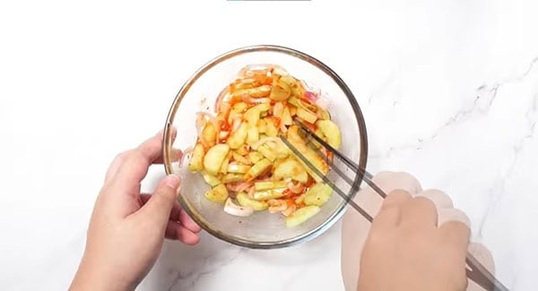 Cucumber, onion and dressing in a bowl being mixed with a tong. 