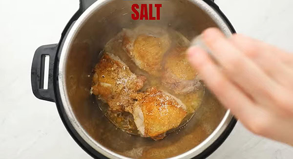 Salt being added to the pot with the brown sugar garlic sauce chicken thighs. 