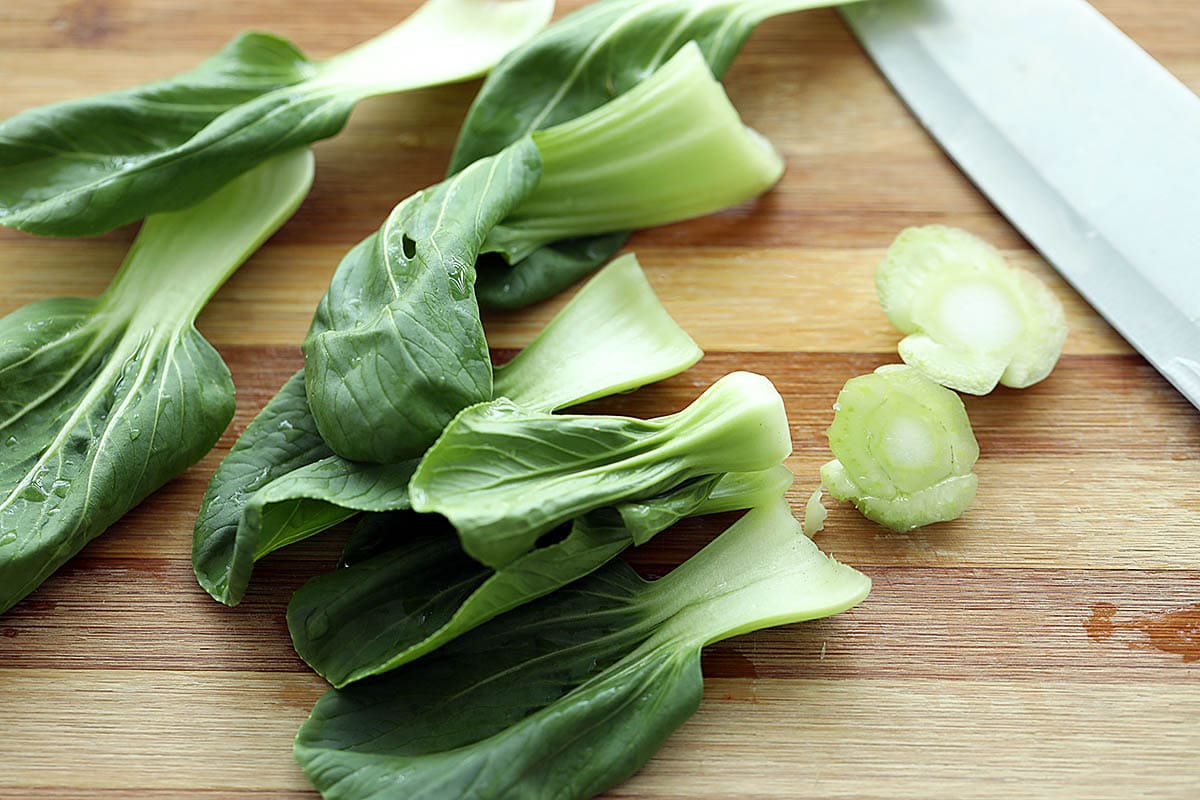 Cutting the bottom stem of bok choy on a cutting board. 