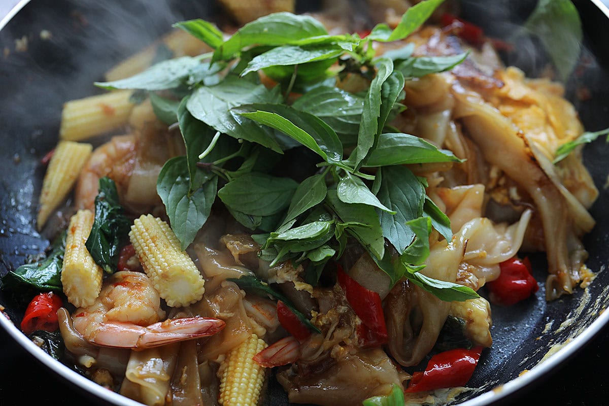 Adding basil to Pad Kee Mao in a skillet. 