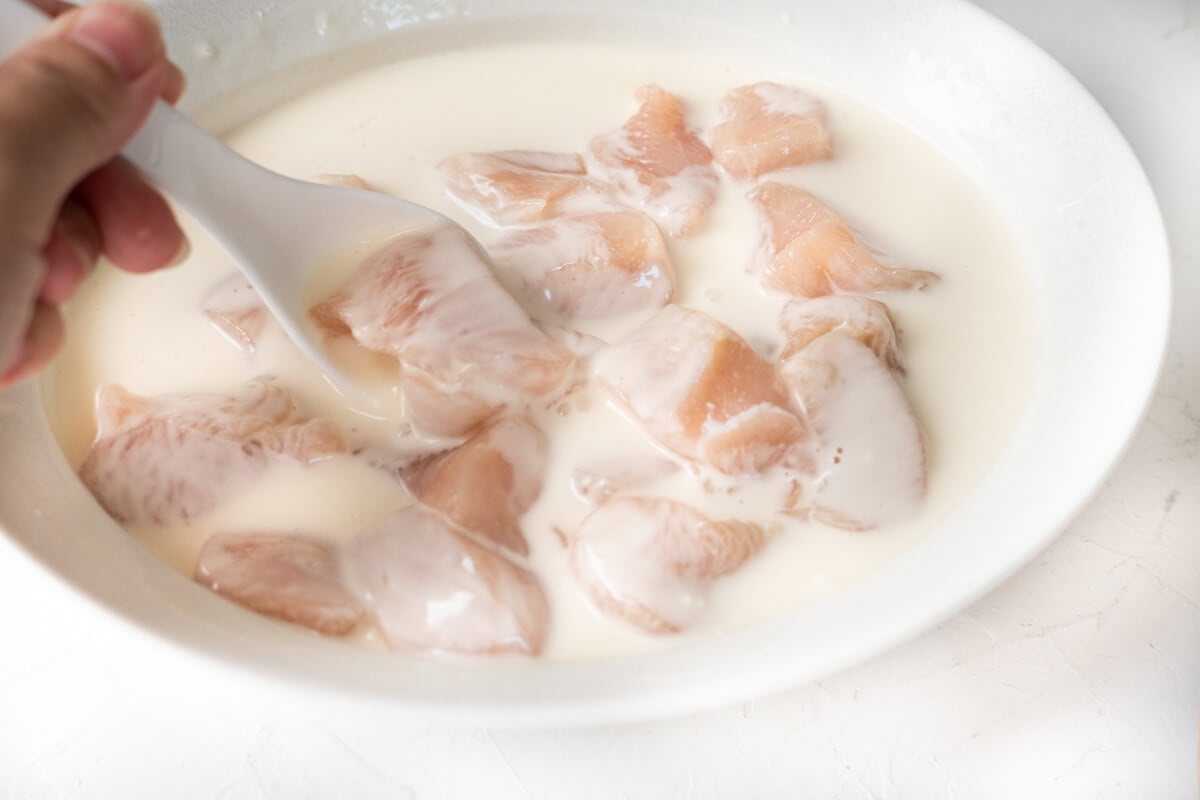 Coating chicken cubes with frying batter in a shallow bowl. 