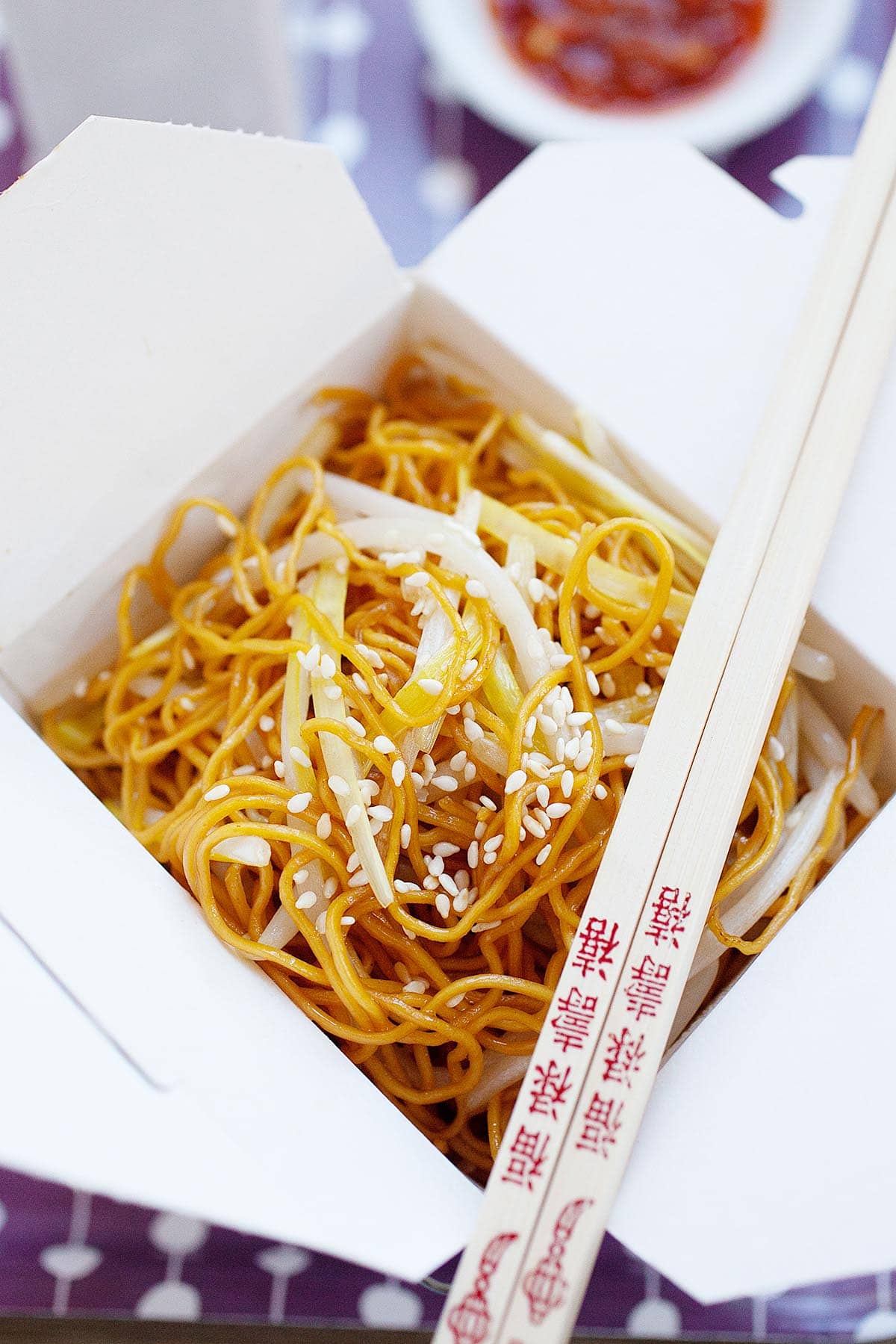 Hong Kong chow mein served in a takeout box with a pair of chopsticks. 