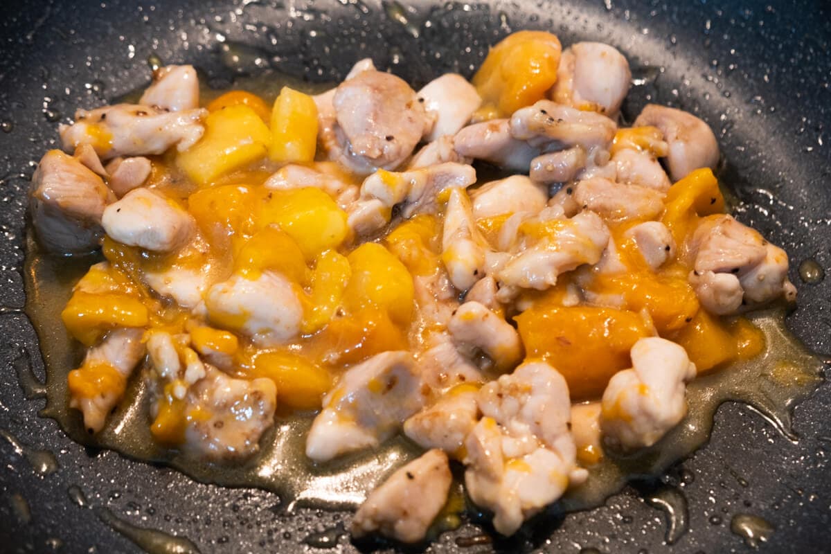 Chicken thighs and mango cubes in a skillet.