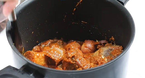 Coated beef cubes and spices mixed in a pot using a spatula.