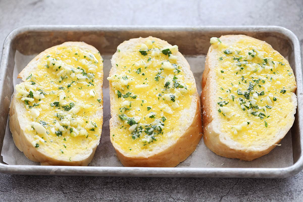 French bread slices spread with garlic butter, ready for toasting.